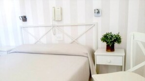 Una habitación de hotel con una cama, una mesita de noche, una silla y una pequeña planta en maceta.