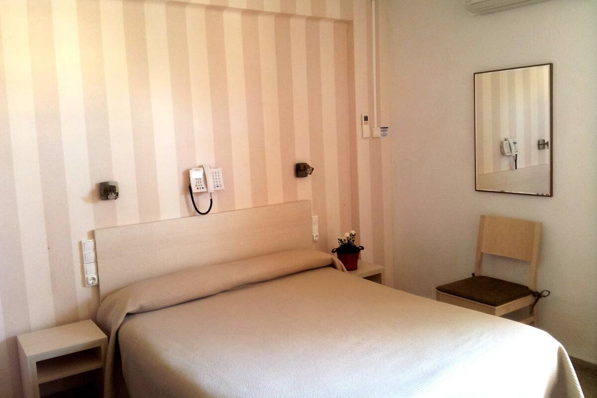 Habitación de hotel con pared a rayas, cama, mesita de noche, silla, espejo y teléfono.