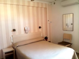 Habitación de hotel con pared a rayas, cama, mesita de noche, silla, espejo y teléfono.