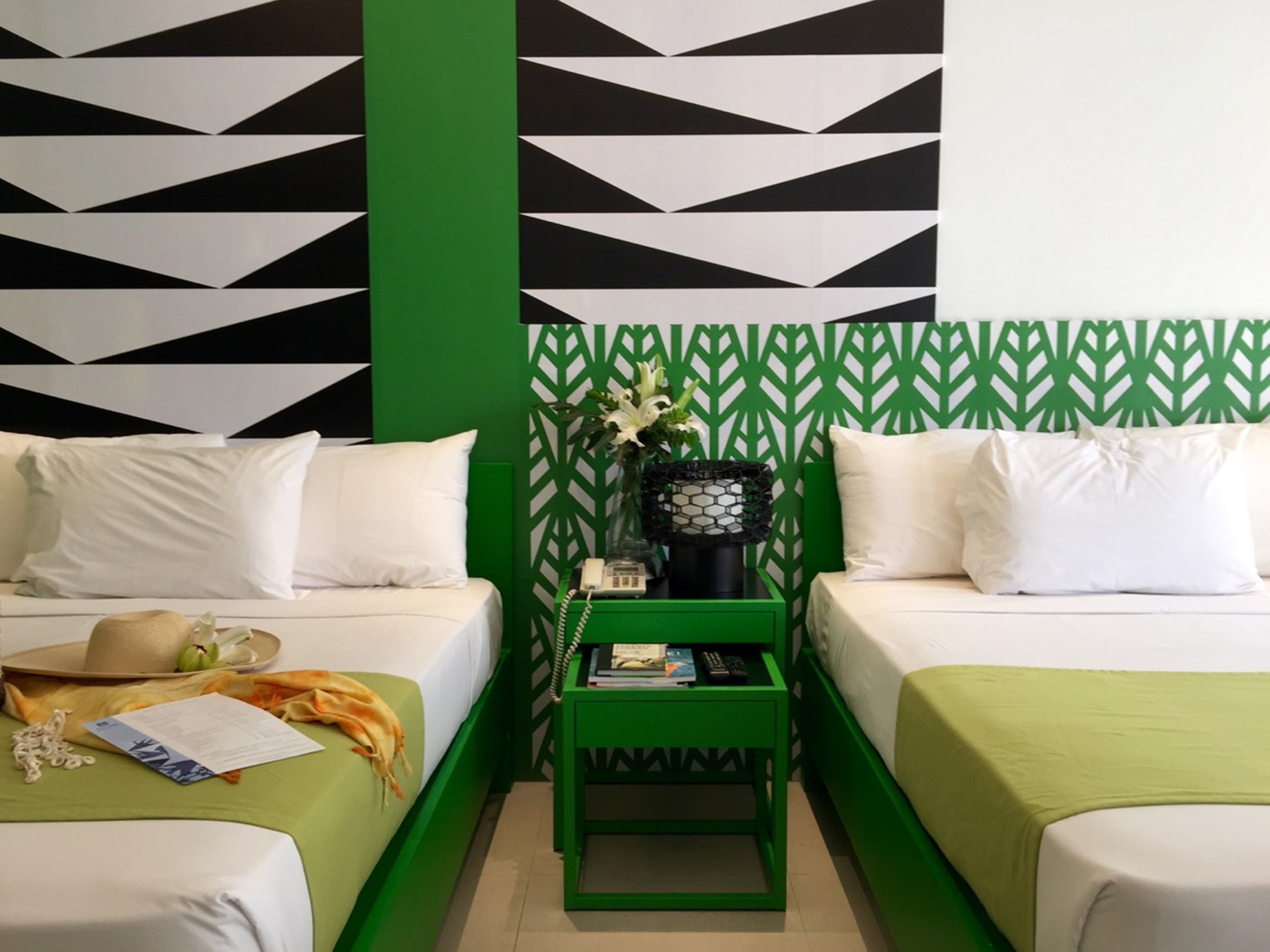 Ein Hotelzimmer mit zwei Betten, einem grünen Nachttisch und einer Wand mit Muster.