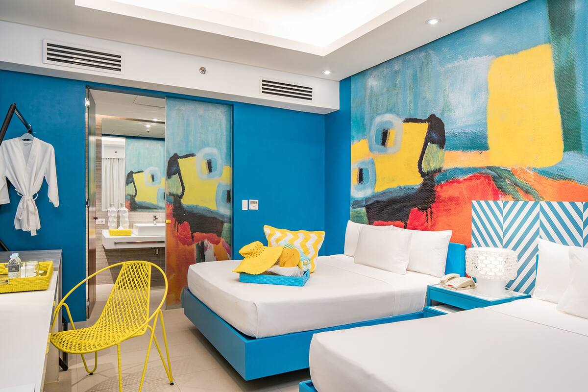 Una habitación de hotel moderna con una cama grande, un escritorio pequeño, una silla y un baño visible a través de una puerta abierta.