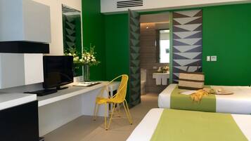 A modern hotel room with a bed, a desk with a TV, a chair, and a bathroom visible through an open door.