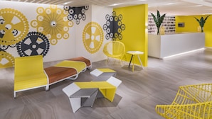 Un espace d’accueil moderne, avec un mobilier jaune et blanc, comprenant un comptoir d’accueil, des chaises et un coin salon aux motifs géométriques.