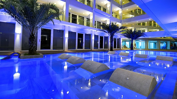 Une piscine intérieure à plusieurs niveaux, à l’eau cristalline, entourée de palmiers et bordée d’une architecture moderne.