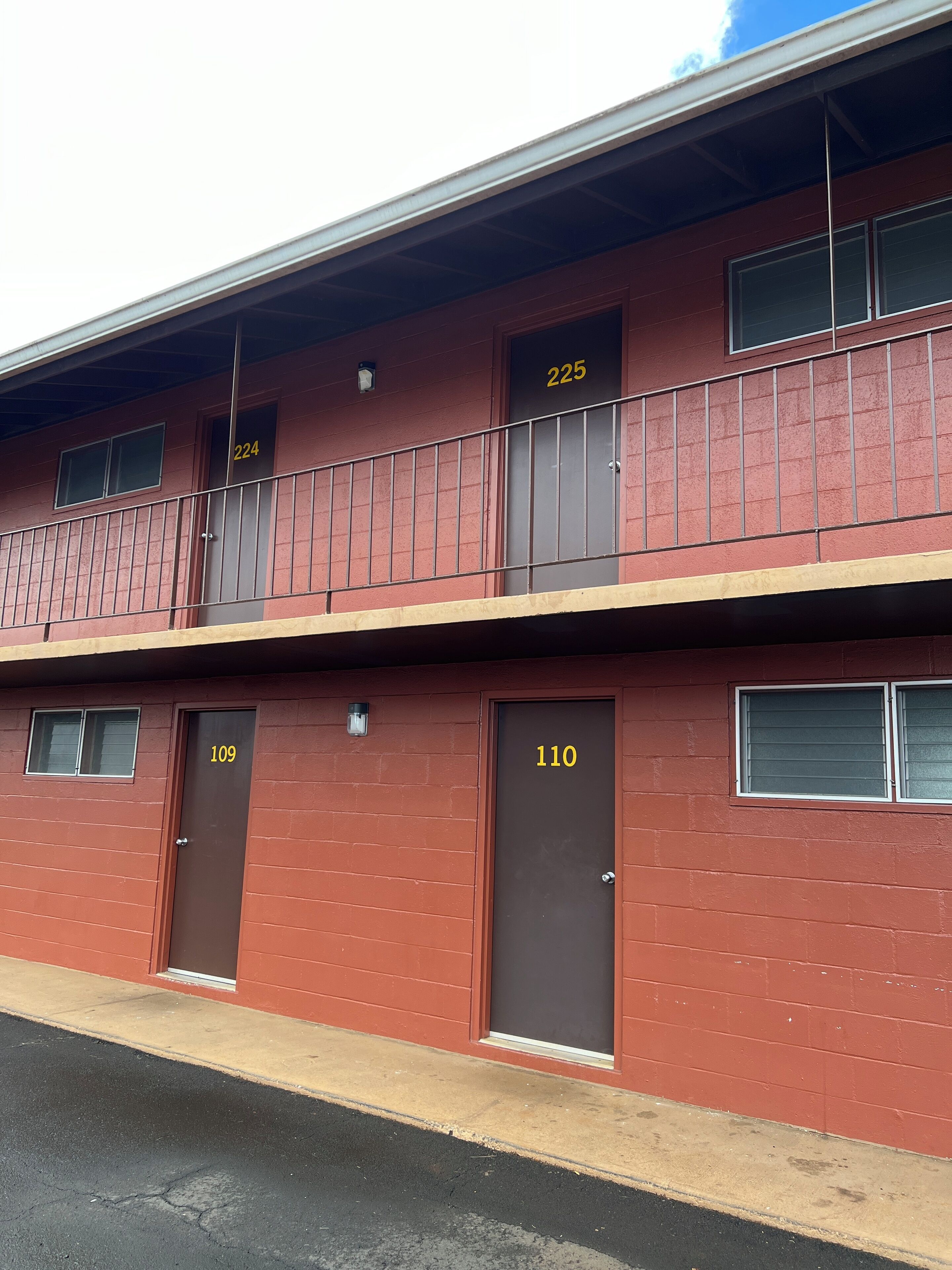 A red brick building with numbered doors, a balcony, and a visible window.
