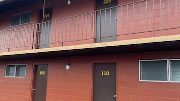 A red brick building with numbered doors, a balcony, and a visible window.