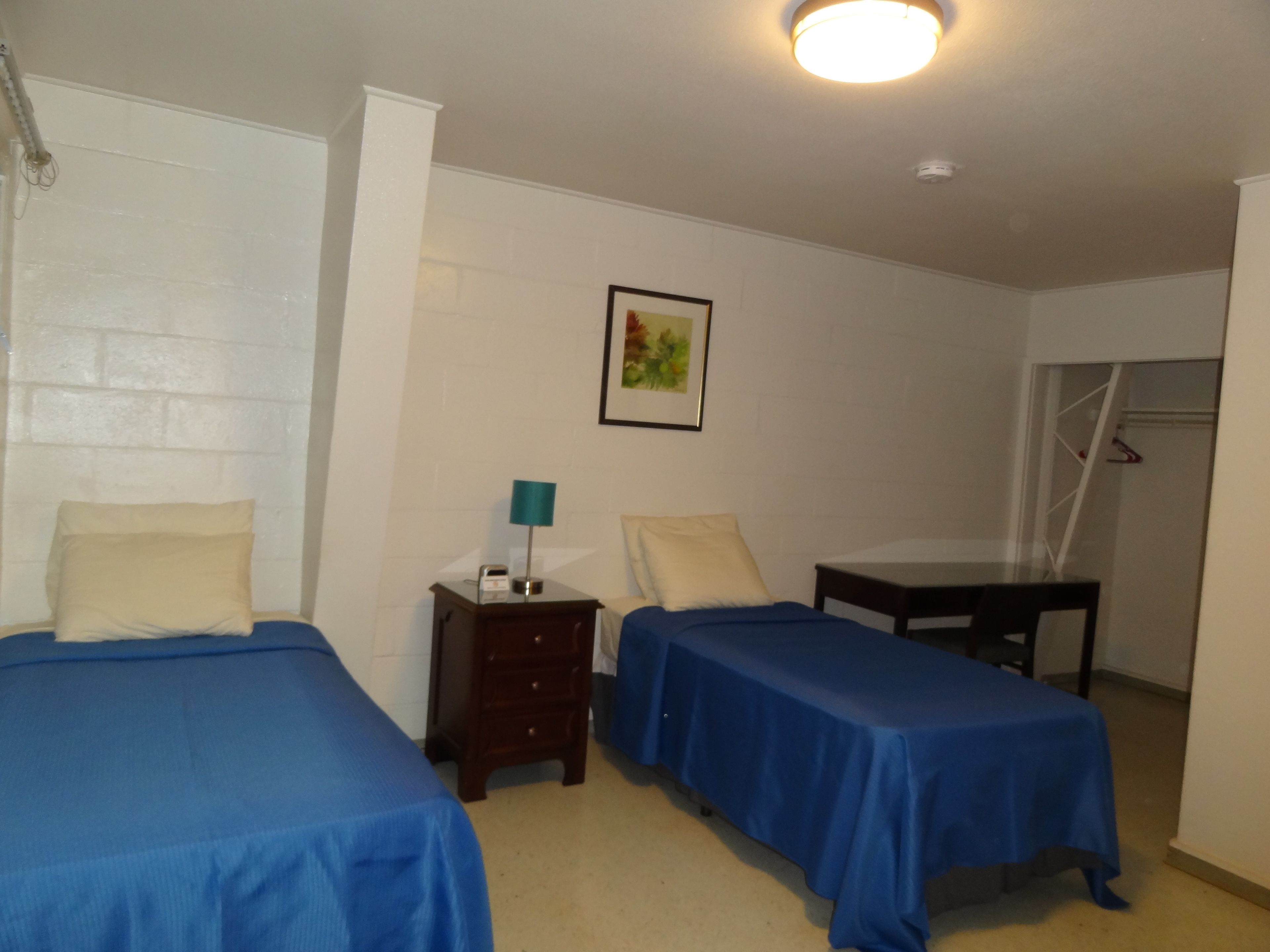 A room with two beds, a nightstand, a table, and a wall-mounted picture.
