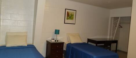 A room with two beds, a nightstand, a table, and a wall-mounted picture.