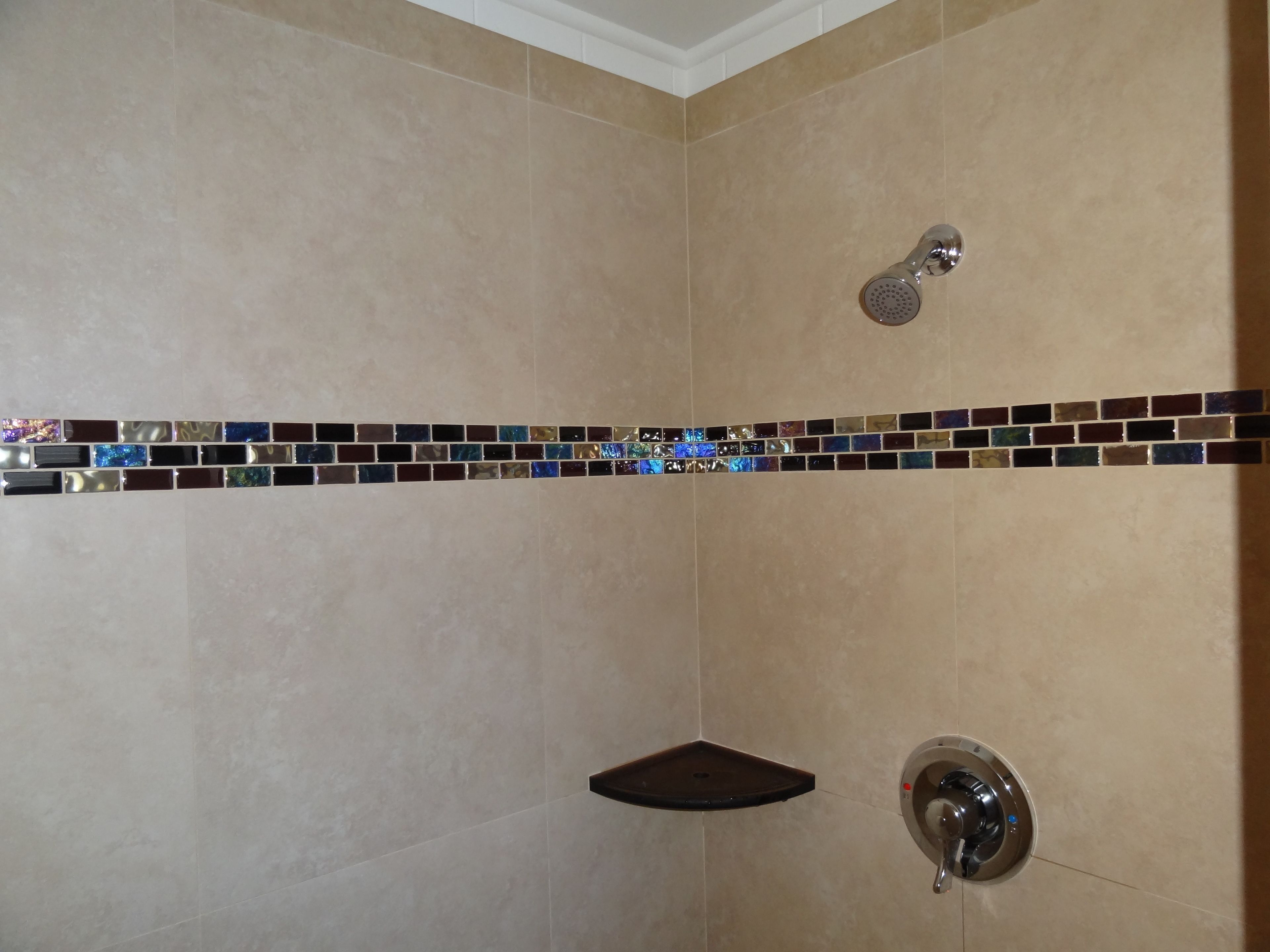 A shower with a handheld showerhead, a corner shelf, and a wall-mounted faucet.
