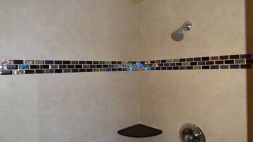 A shower with a handheld showerhead, a corner shelf, and a wall-mounted faucet.