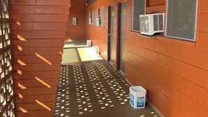A corridor with a brick wall on one side and air conditioning units mounted on the wall. - Tip Top Motel Cafe & Bakery (Lihue)