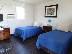 A room with two beds, a desk, a chair, a TV, an air conditioner, and a framed picture on the wall. - Tip Top Motel Cafe & Bakery (Lihue)