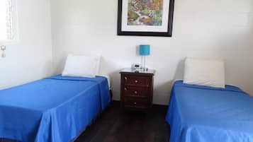 A room with two beds, each with blue bedding, a small wooden nightstand with a lamp, and a framed picture on the wall.
