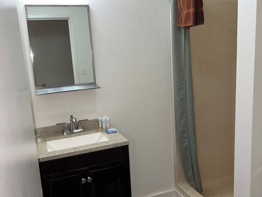 A bathroom with a sink, mirror, dark wooden cabinet, and a shower area with a towel hanging on the door.
