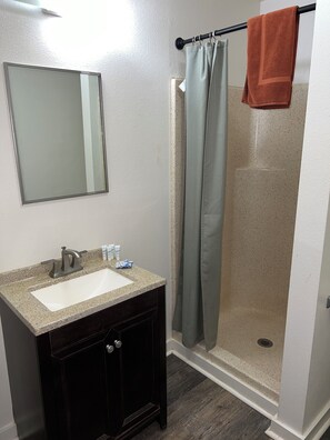 A bathroom with a sink, mirror, dark wooden cabinet, shower curtain, and a towel hanging on the shower rod. - Tip Top Motel Cafe & Bakery (Lihue)