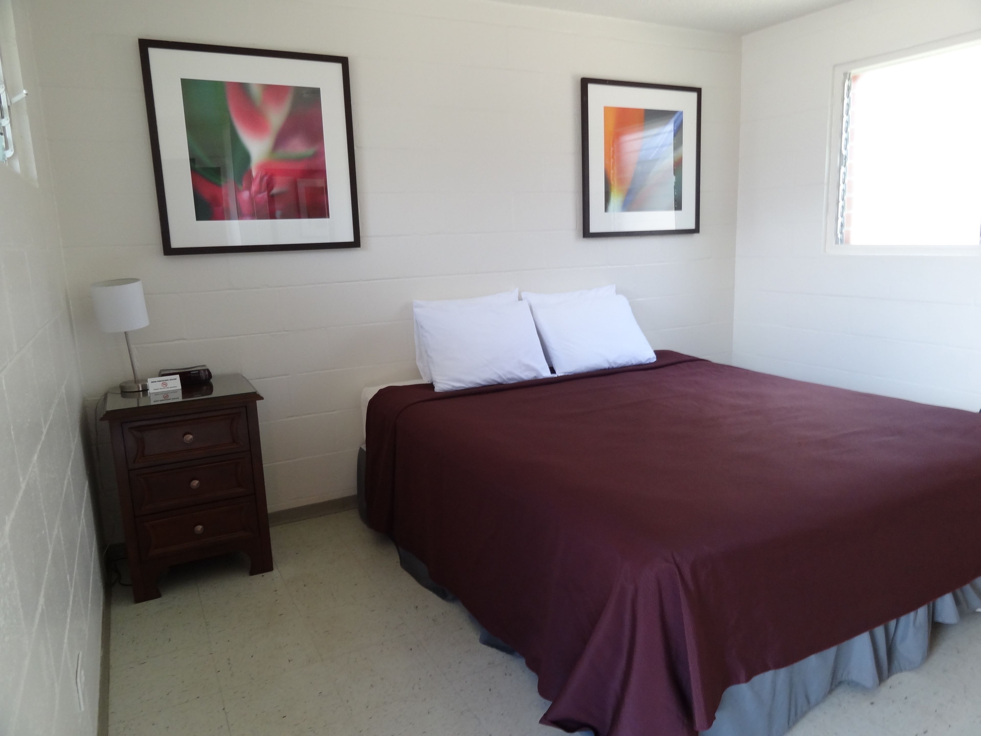 Un dormitorio con una cama grande, una mesita de noche, una lámpara y dos cuadros en la pared.
