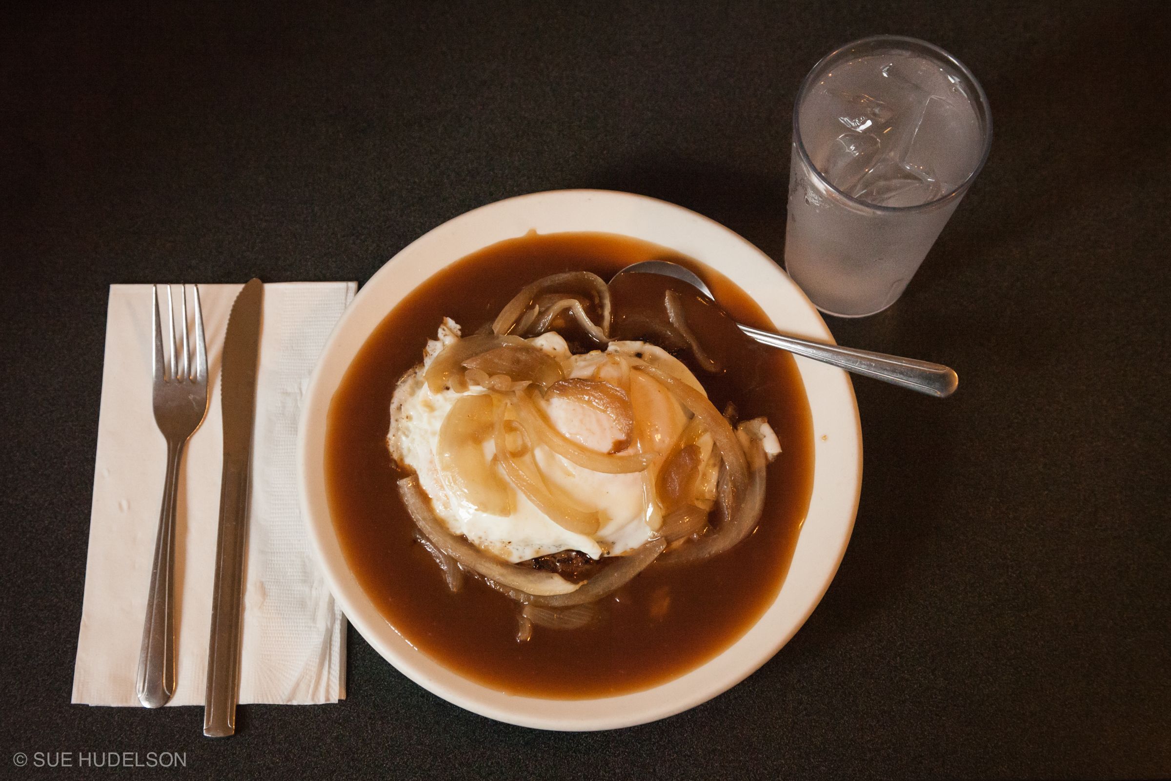A bowl of soup with a spoon and a glass of water on a table.