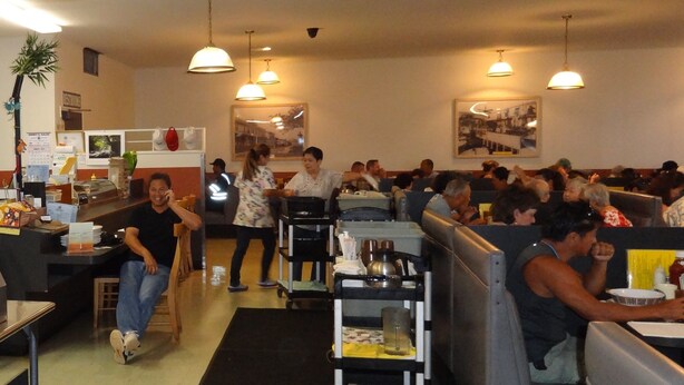 A restaurant with booths and tables, a counter, and hanging lights. - Tip Top Motel Cafe & Bakery (Lihue)