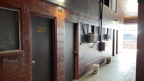 A hallway with numbered doors, a trash bin, and a ceiling light. - Tip Top Motel Cafe & Bakery (Lihue)