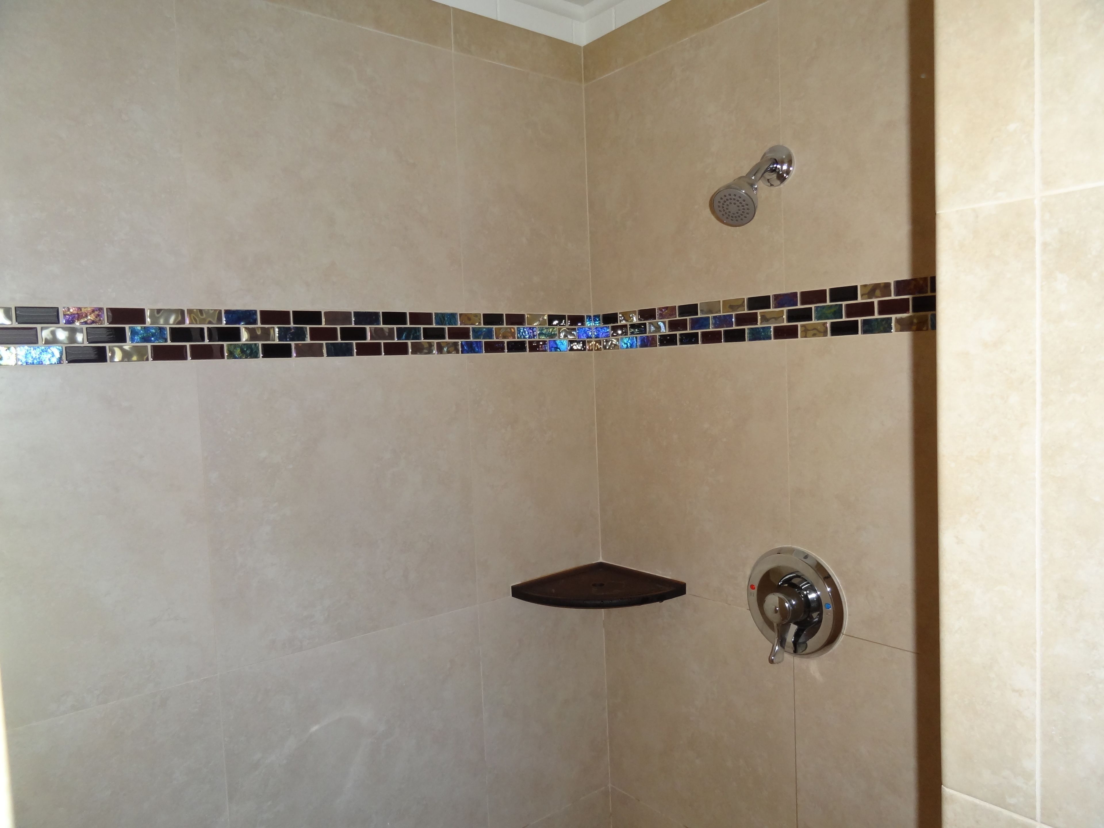 A shower area with beige tiles, a showerhead, and a shelf.
