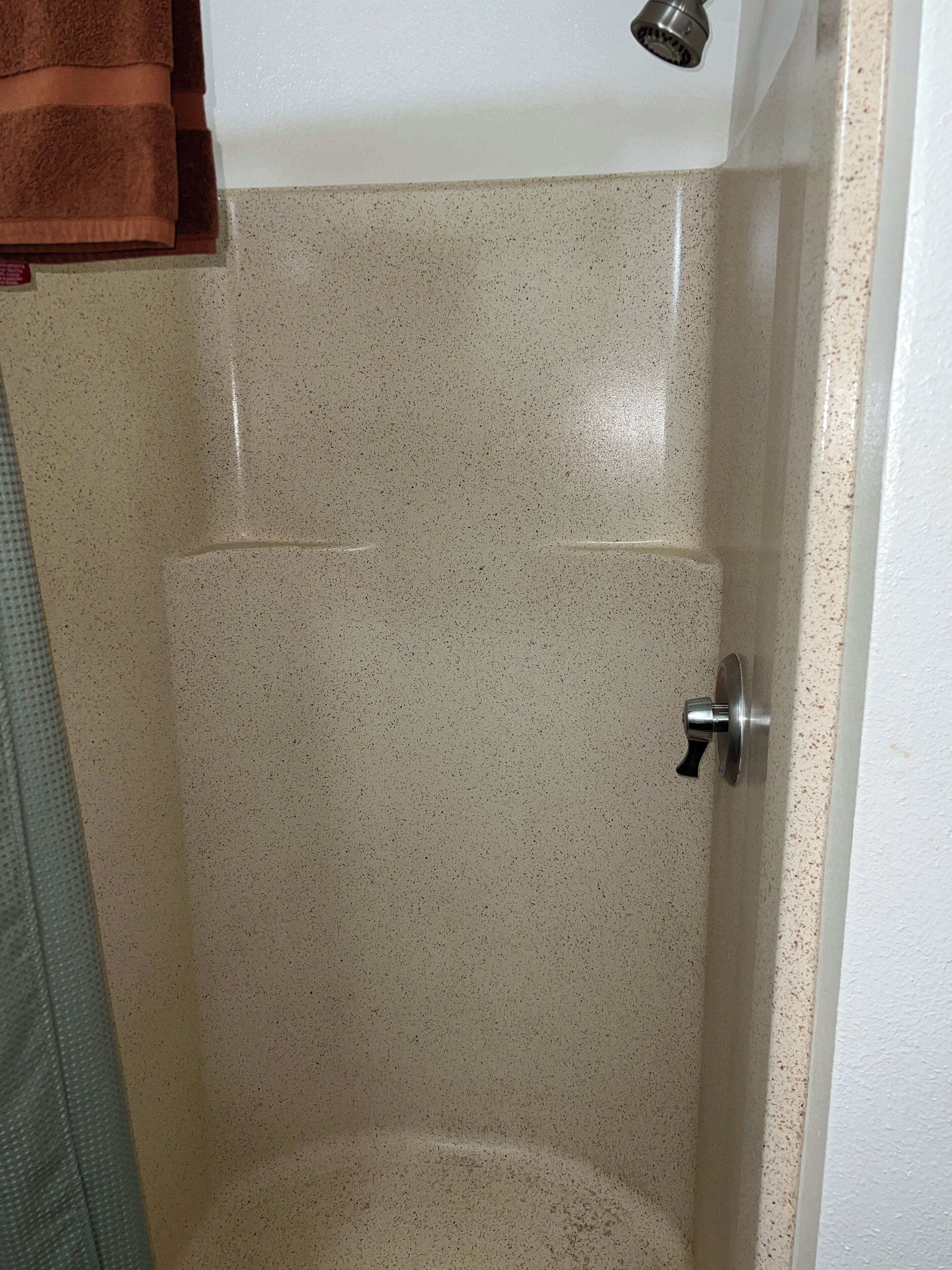 Ein Badezimmer mit einer Wand aus gesprenkelten Fliesen, einer Duschbrause und einem Türgriff.