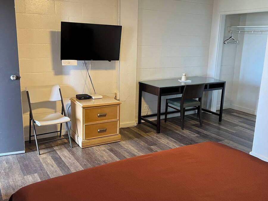 Una habitación con cama, escritorio, silla, televisor montado en la pared y cómoda.