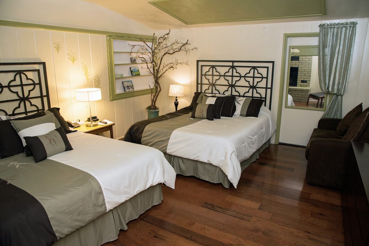 A room with two beds, a nightstand, a lamp, a potted plant, and a mirror.