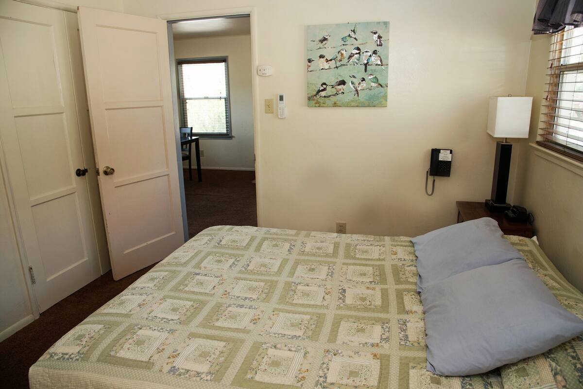 A bedroom with a bed, a painting, a lamp, and a telephone on the wall.