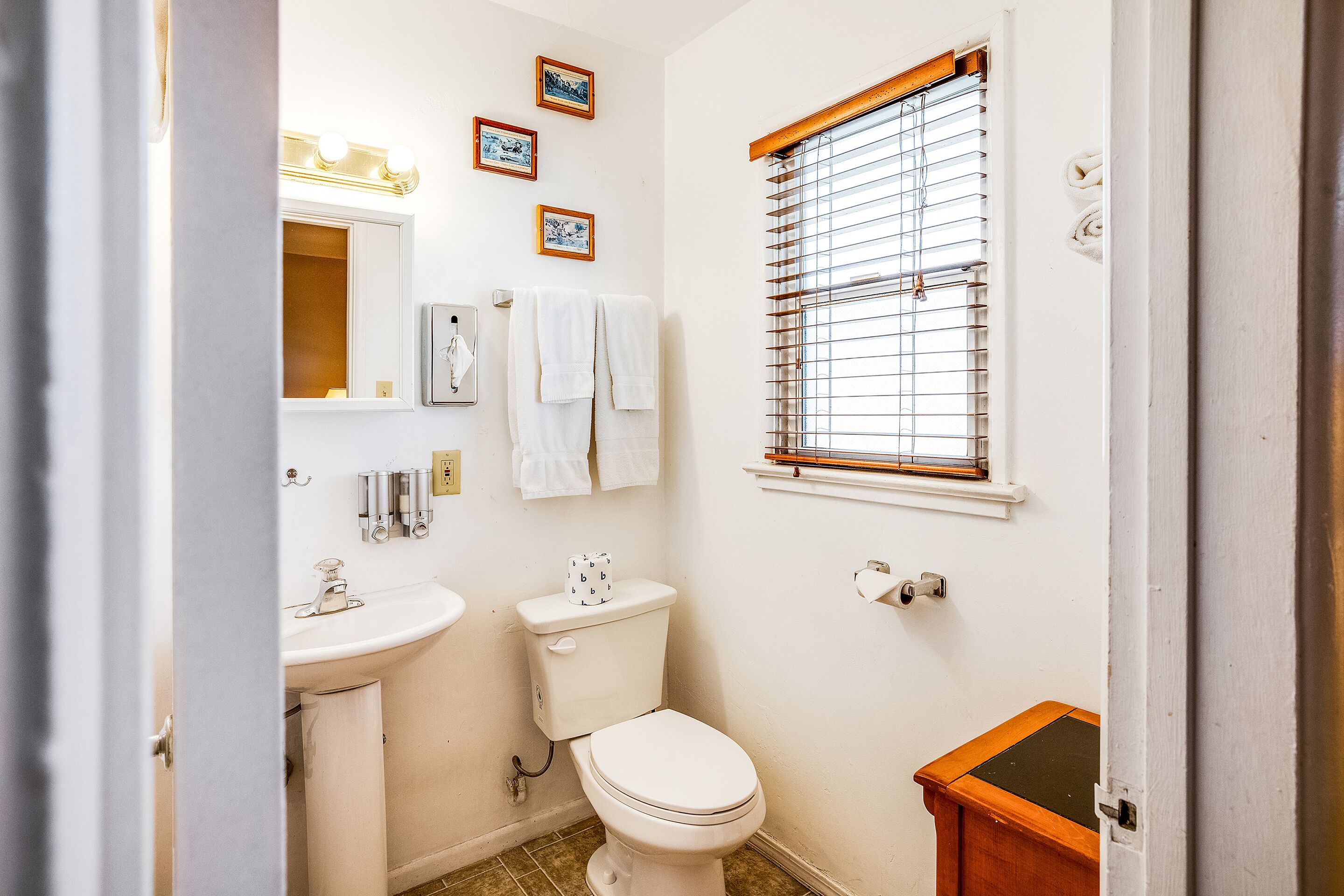 A bathroom with a toilet, sink, vanity, and a window with blinds.