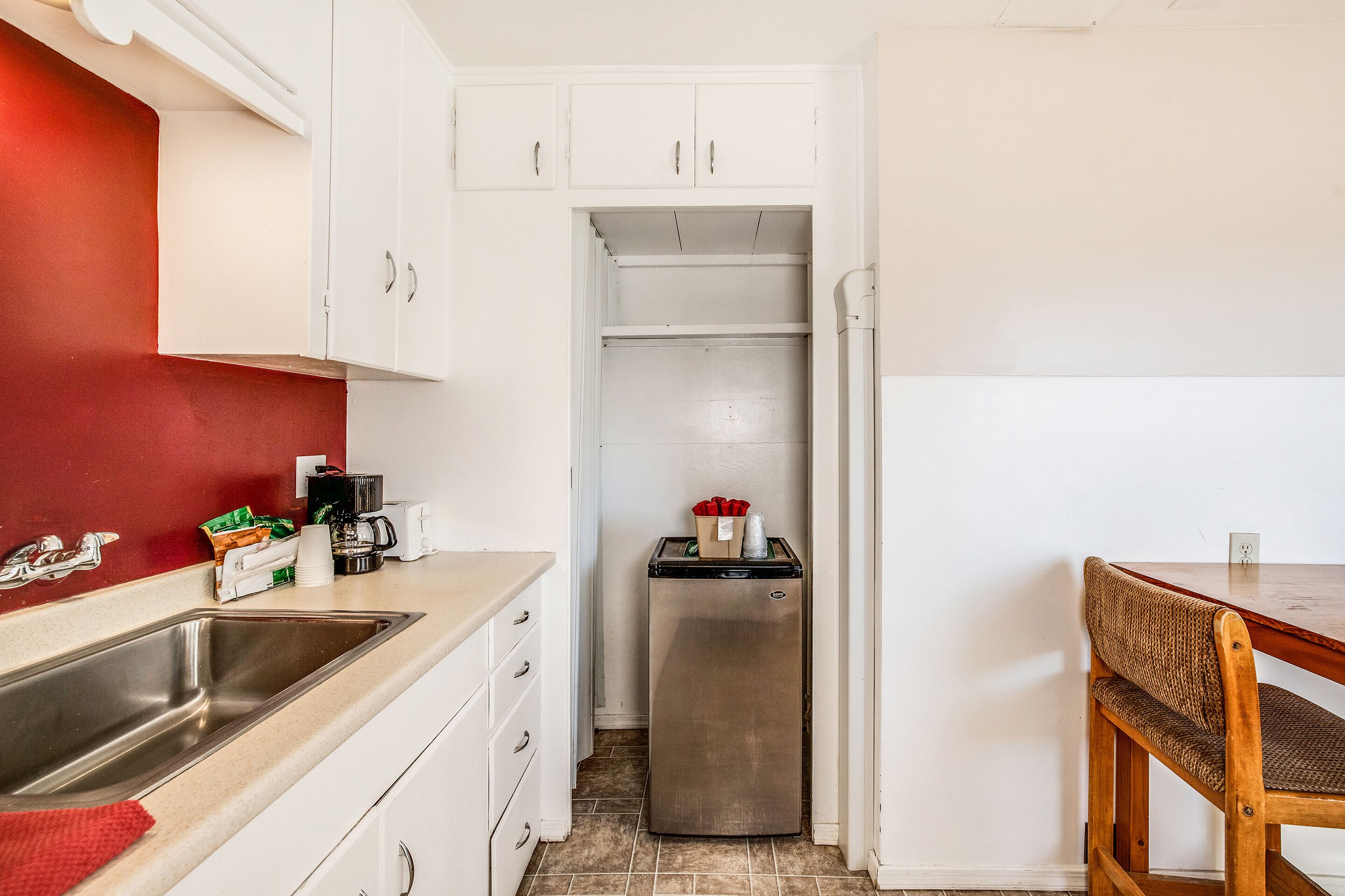 A compact kitchen with white cabinets, a stainless steel sink, and a refrigerator.