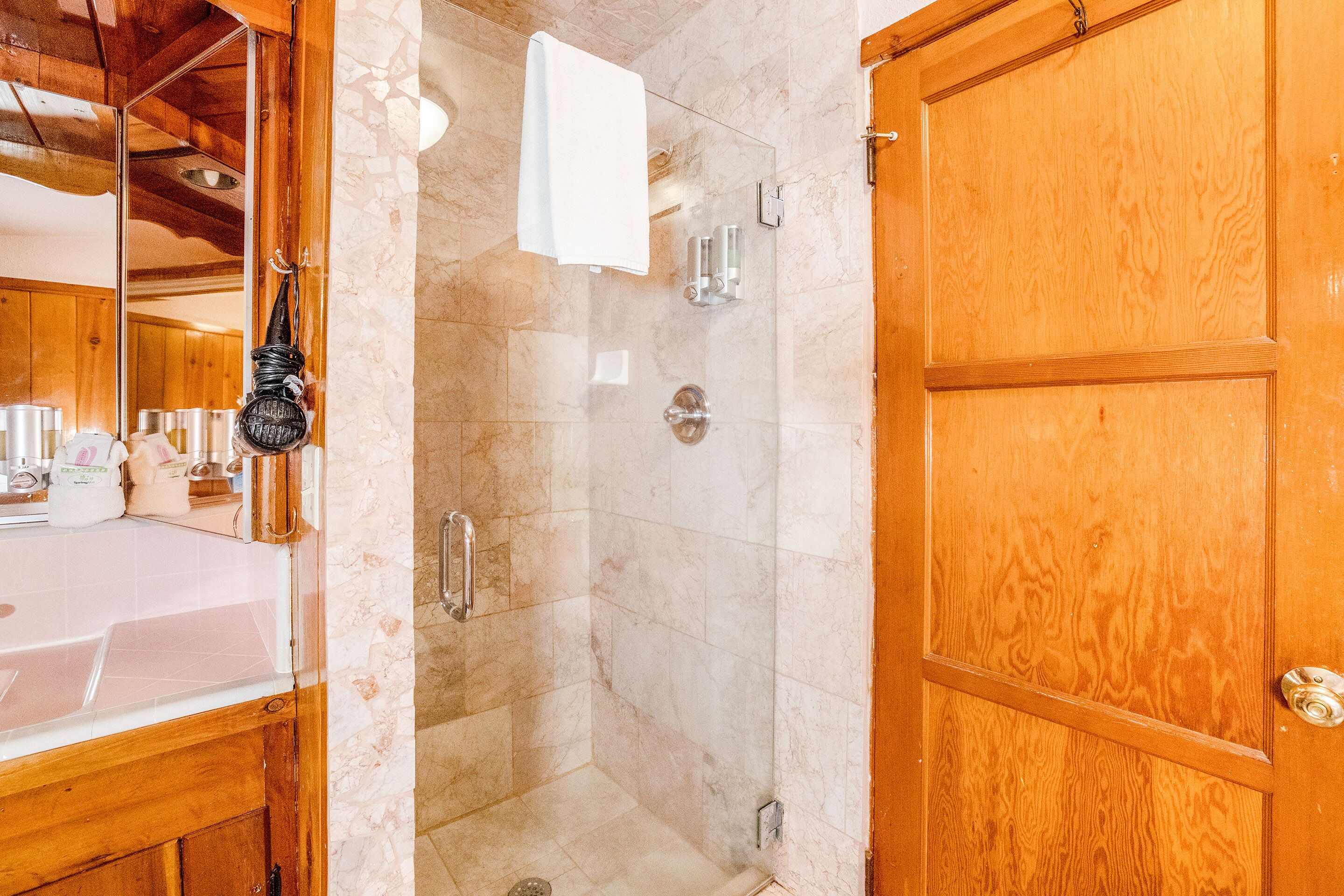 Casa de banho com porta de madeira, cabine de duche em vidro e zona de lavatório com artigos de higiene pessoal.