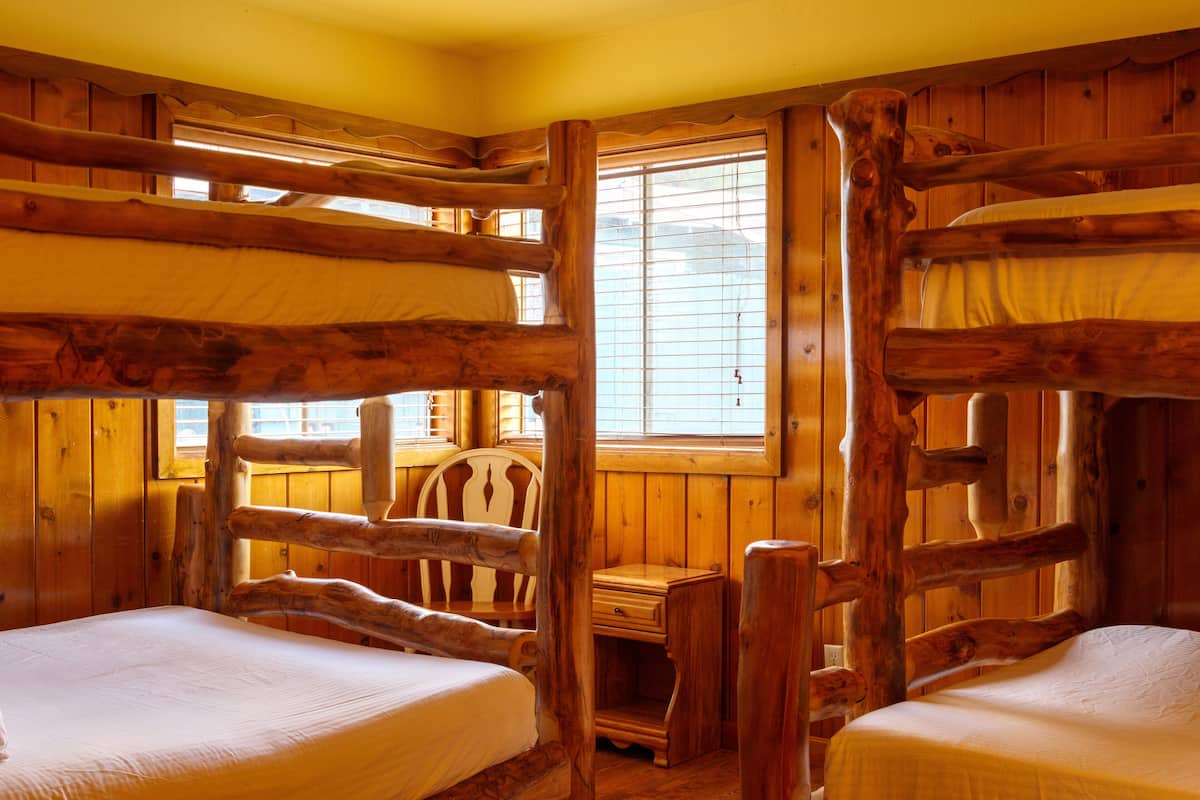 A cabin with wooden walls and a window. There are two beds with white linens.