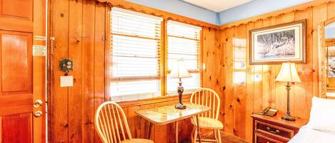 A wooden-paneled room with a bed, a table with chairs, a lamp, and a framed picture on the wall.