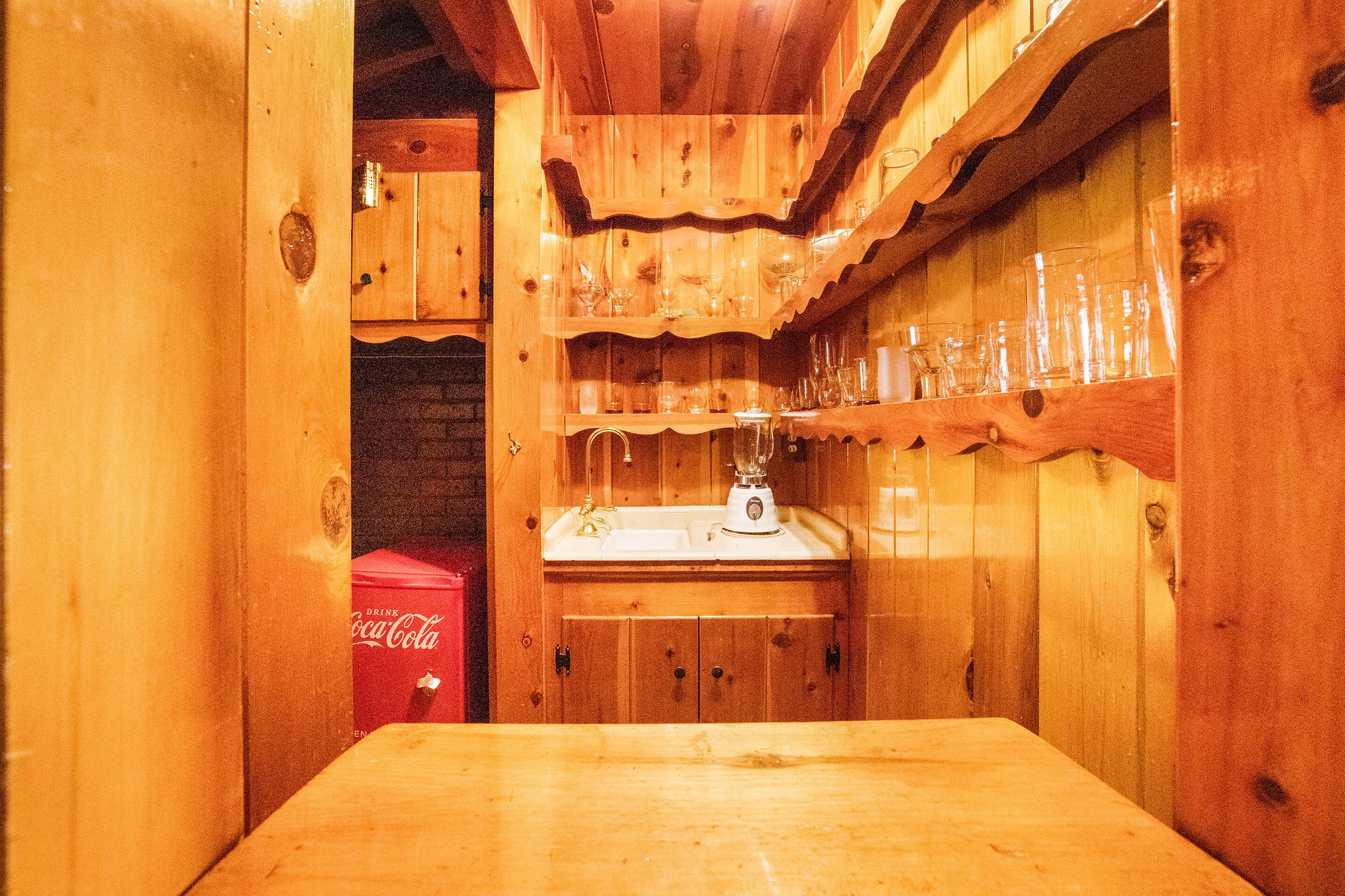 A wooden interior with a wooden table, a sink, and shelves with glasses.