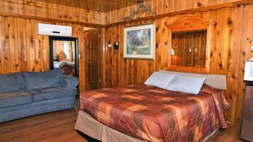 A wooden-paneled room with a bed, a sofa, and an air conditioning unit.