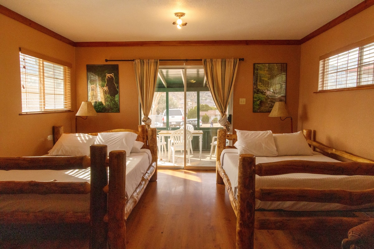 A room with two wooden beds, a table, chairs, and a view through a glass door.