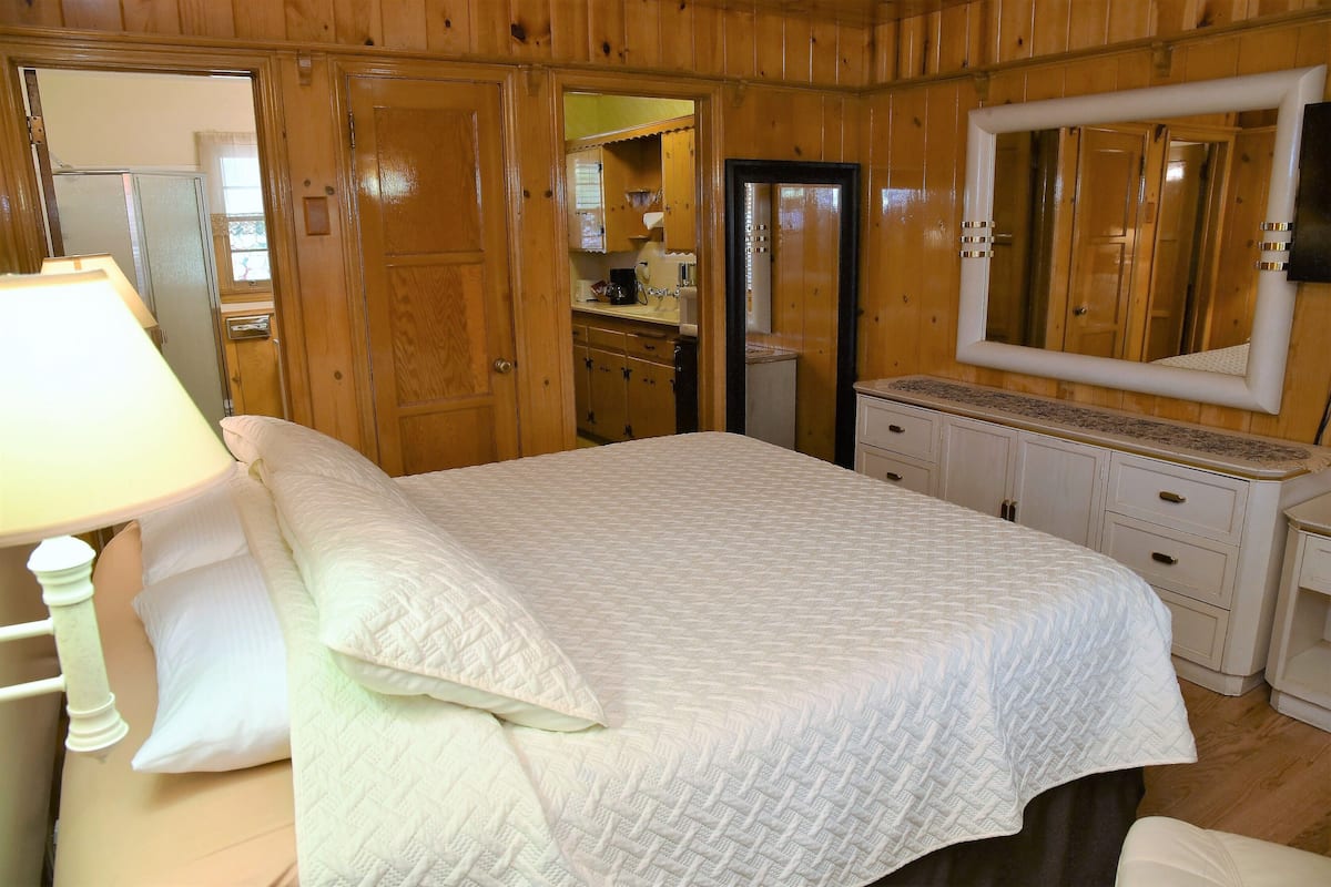 A bedroom with a large bed, a nightstand, a dresser, and a mirror.