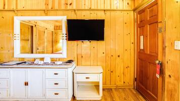 A wooden-paneled room with a white dresser, a mirror, a flat-screen TV, and a wooden door.