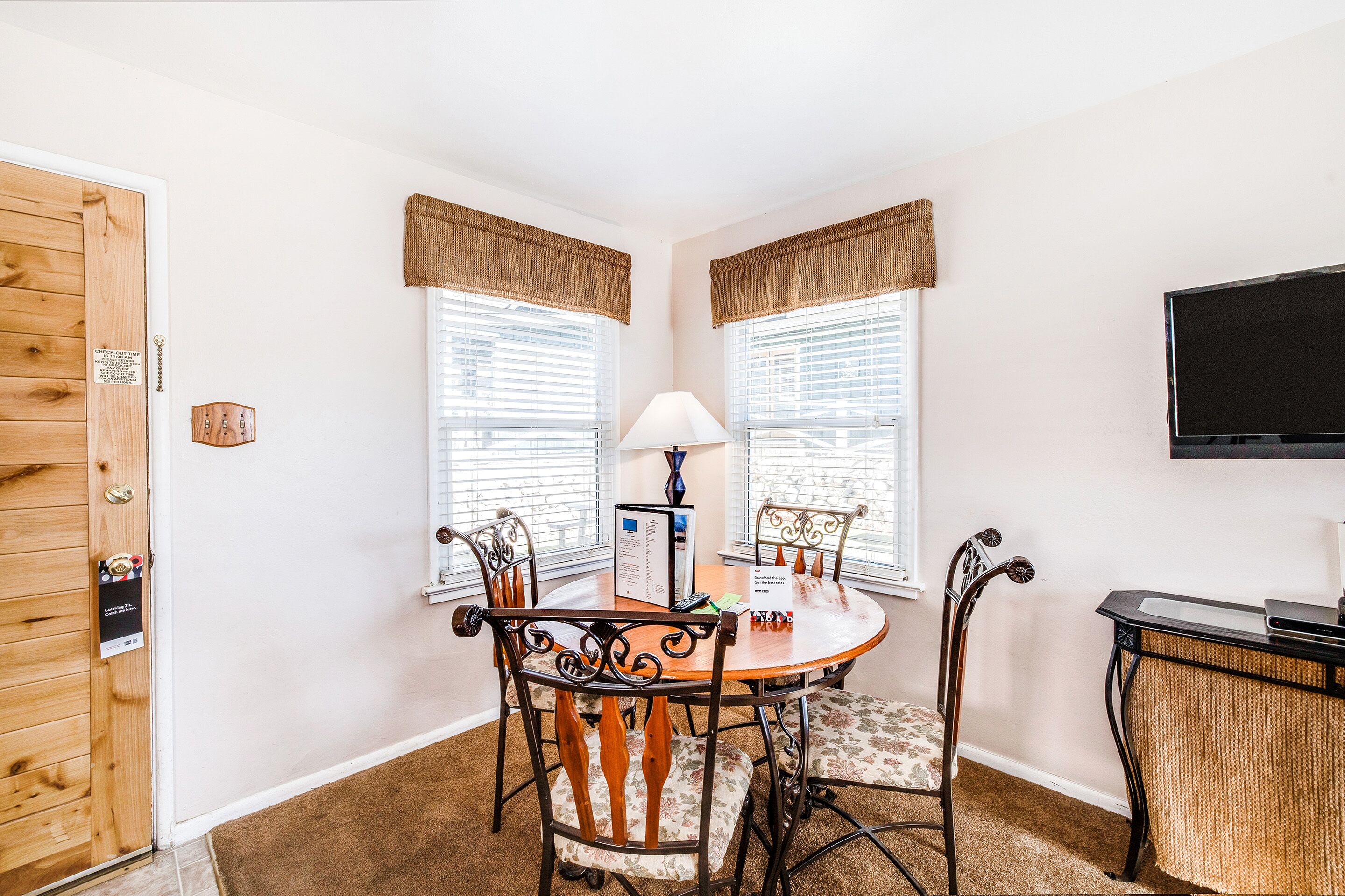 A dining area with a round table, four chairs, a lamp, and a television on the wall.
