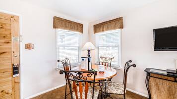 A dining area with a round table, four chairs, a lamp, and a television on the wall.