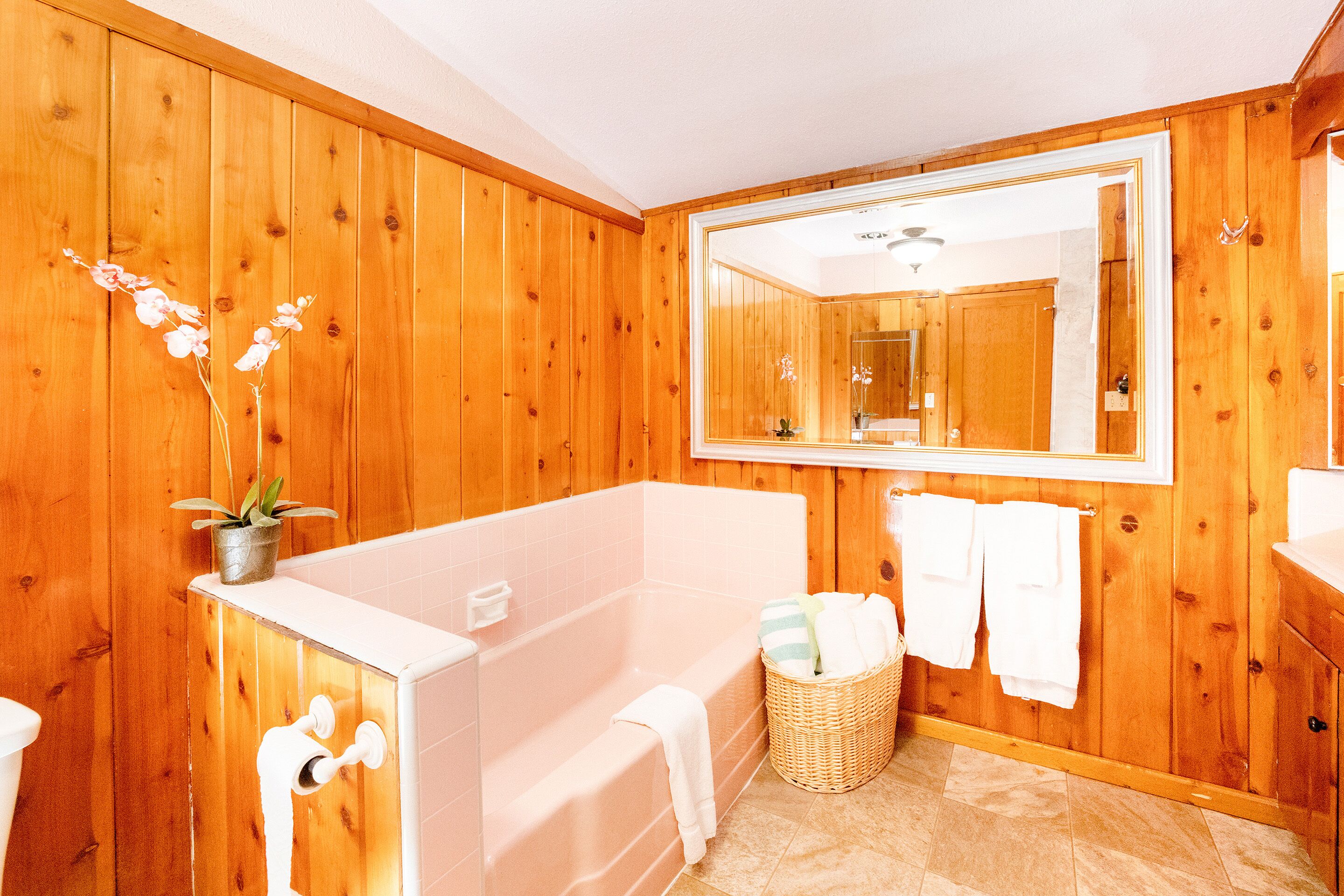 Un baño con paneles de madera, una bañera grande, un espejo, un lavabo y una cesta de mimbre.