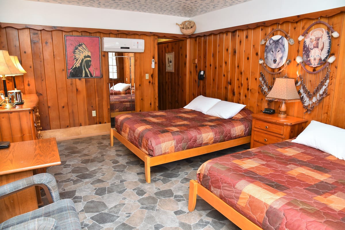 A wooden-paneled room with two beds, a stone floor, a wooden desk, and a chair.