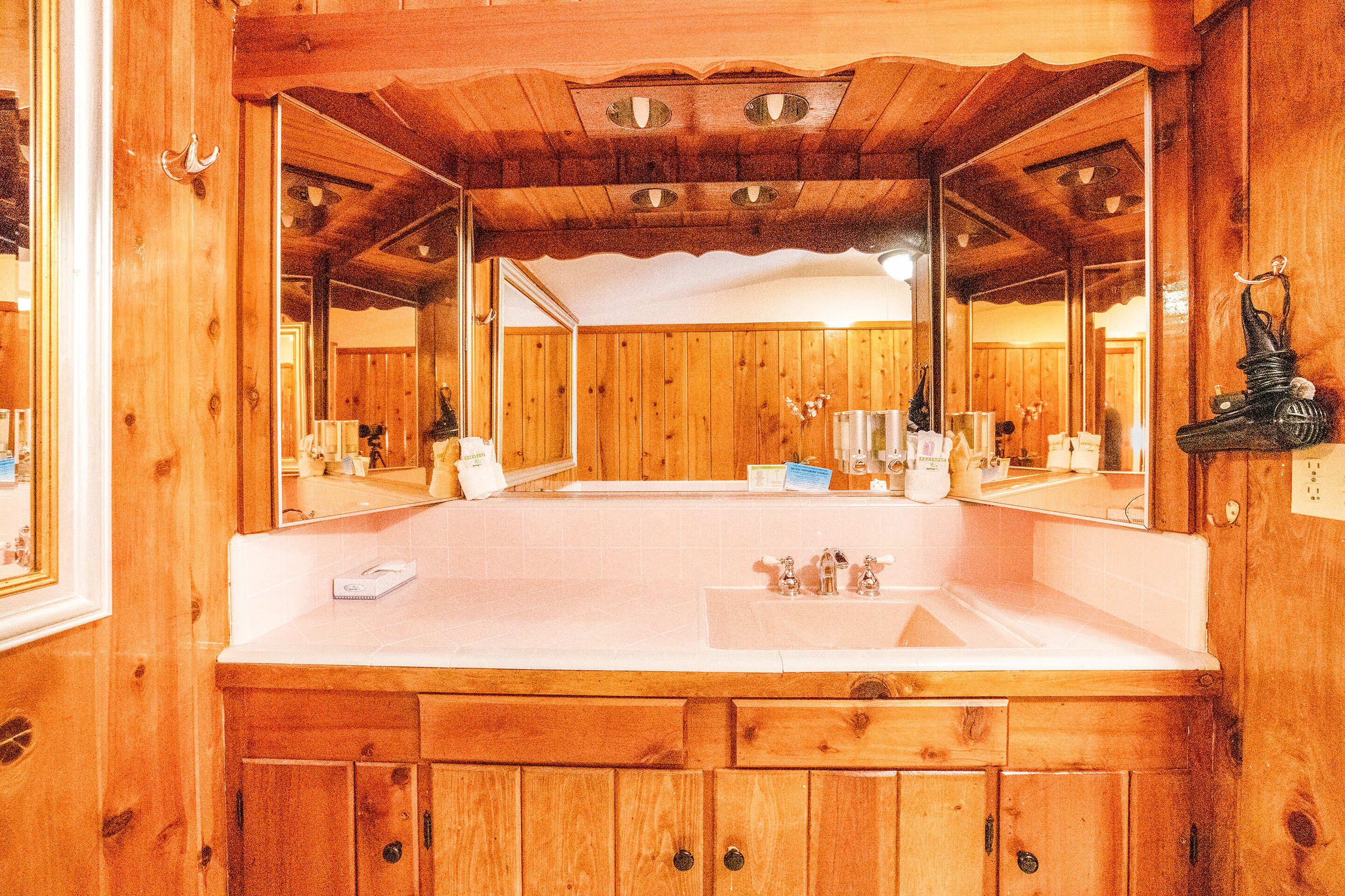 Un baño de madera con un espejo grande, armarios de madera y un lavabo.