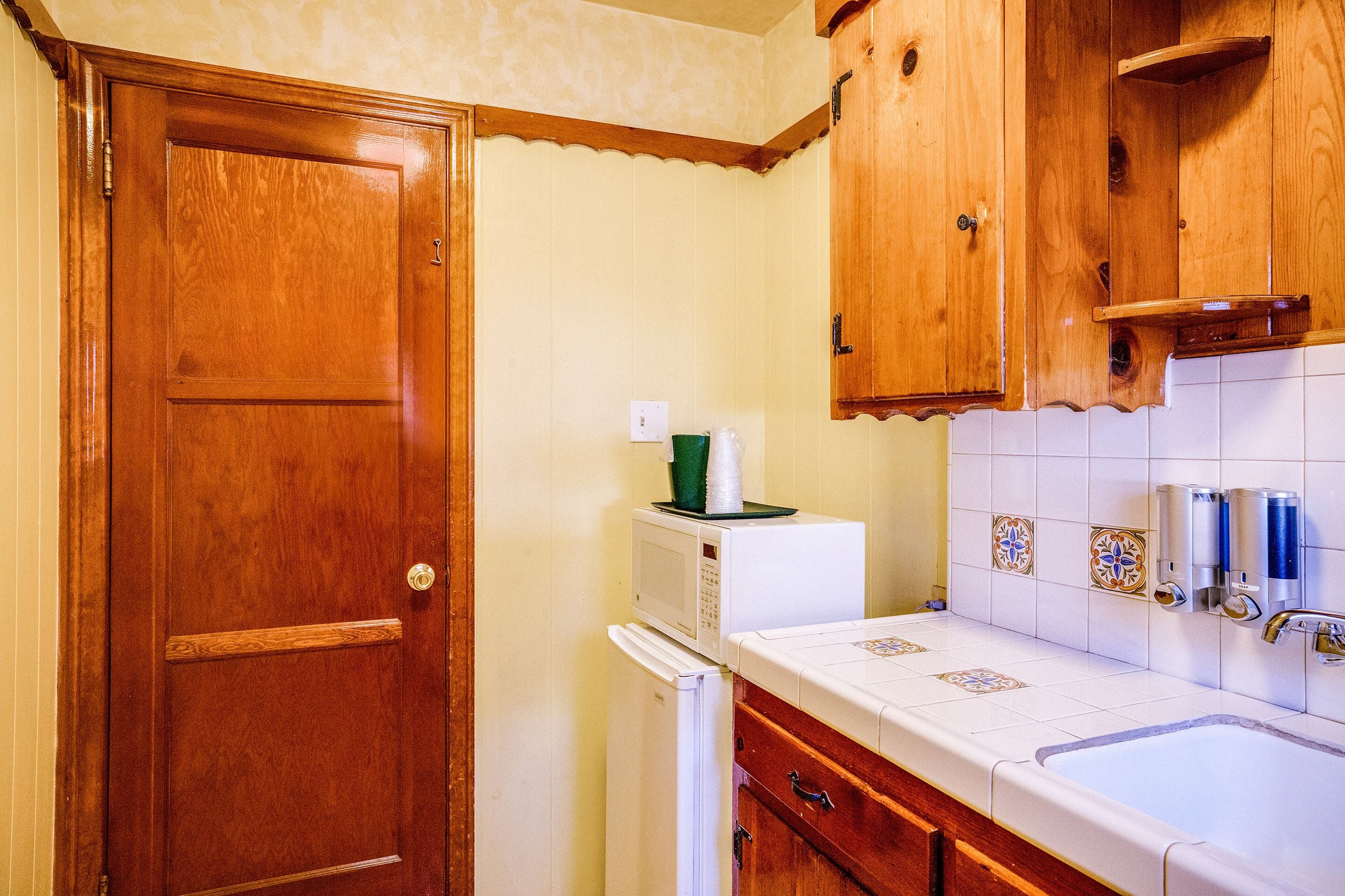 A compact kitchen with wooden cabinets, a white refrigerator, and a tiled backsplash.