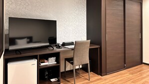 Una habitación moderna con un escritorio de madera oscura, un televisor de pantalla plana, una silla, un refrigerador pequeño y un armario.