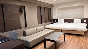 Una habitación de hotel moderna con una cama, un sofá, una mesita pequeña y un escritorio con un control remoto.
