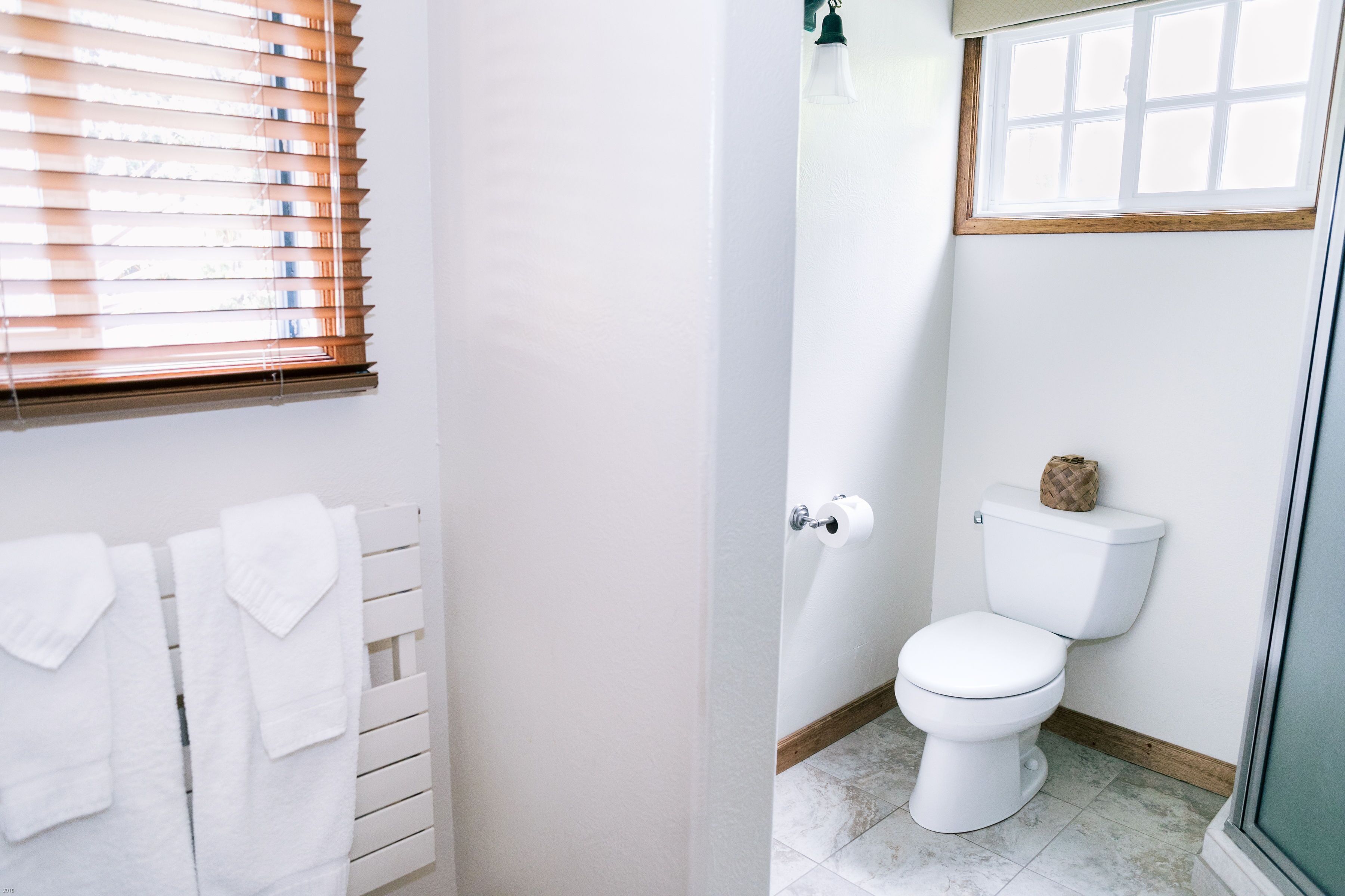 Een badkamer met een toilet, een handdoekrek met handdoeken en een raam met zonwering.
