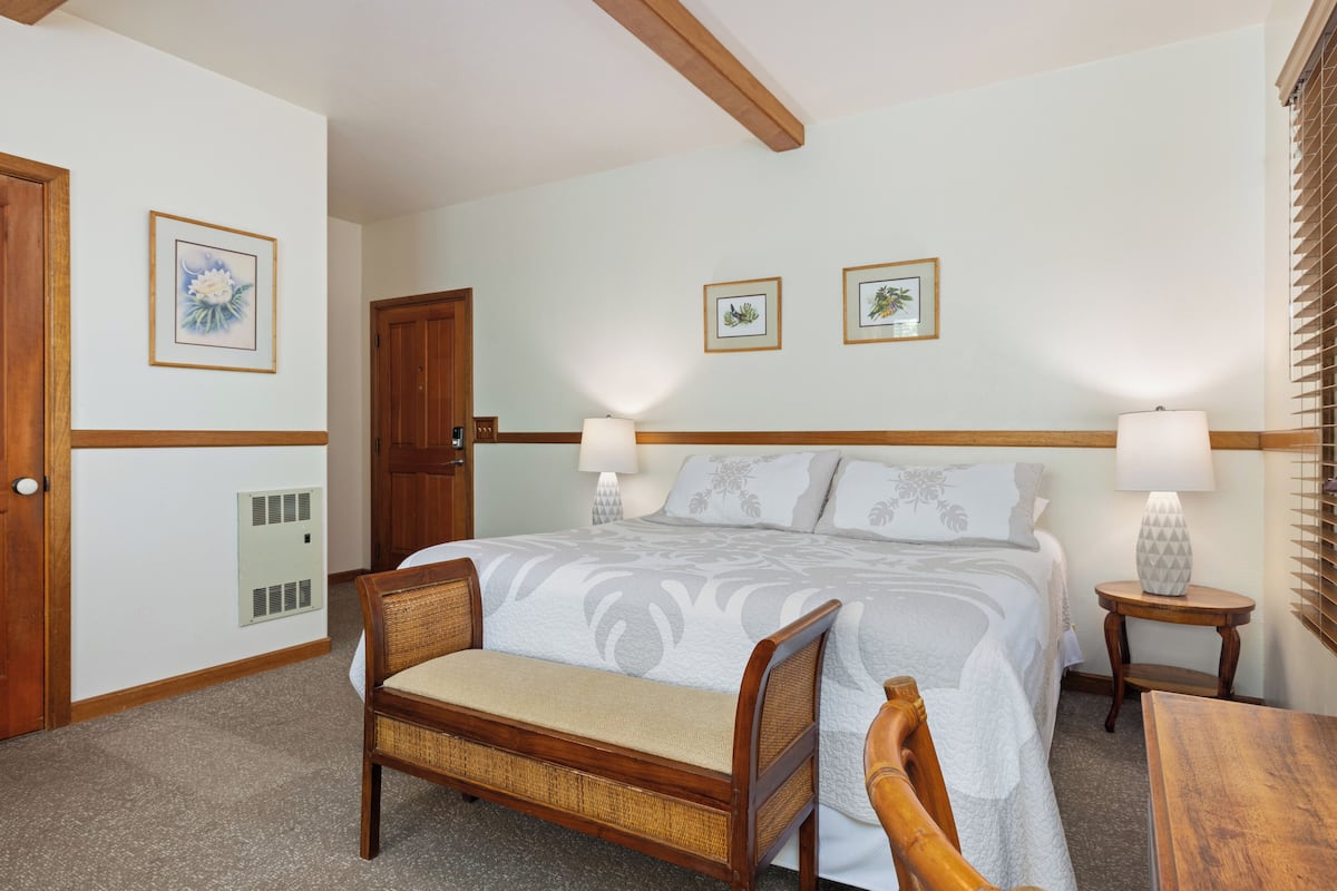 A bedroom with a large bed, two bedside lamps, a wooden bench, and two framed pictures on the wall.