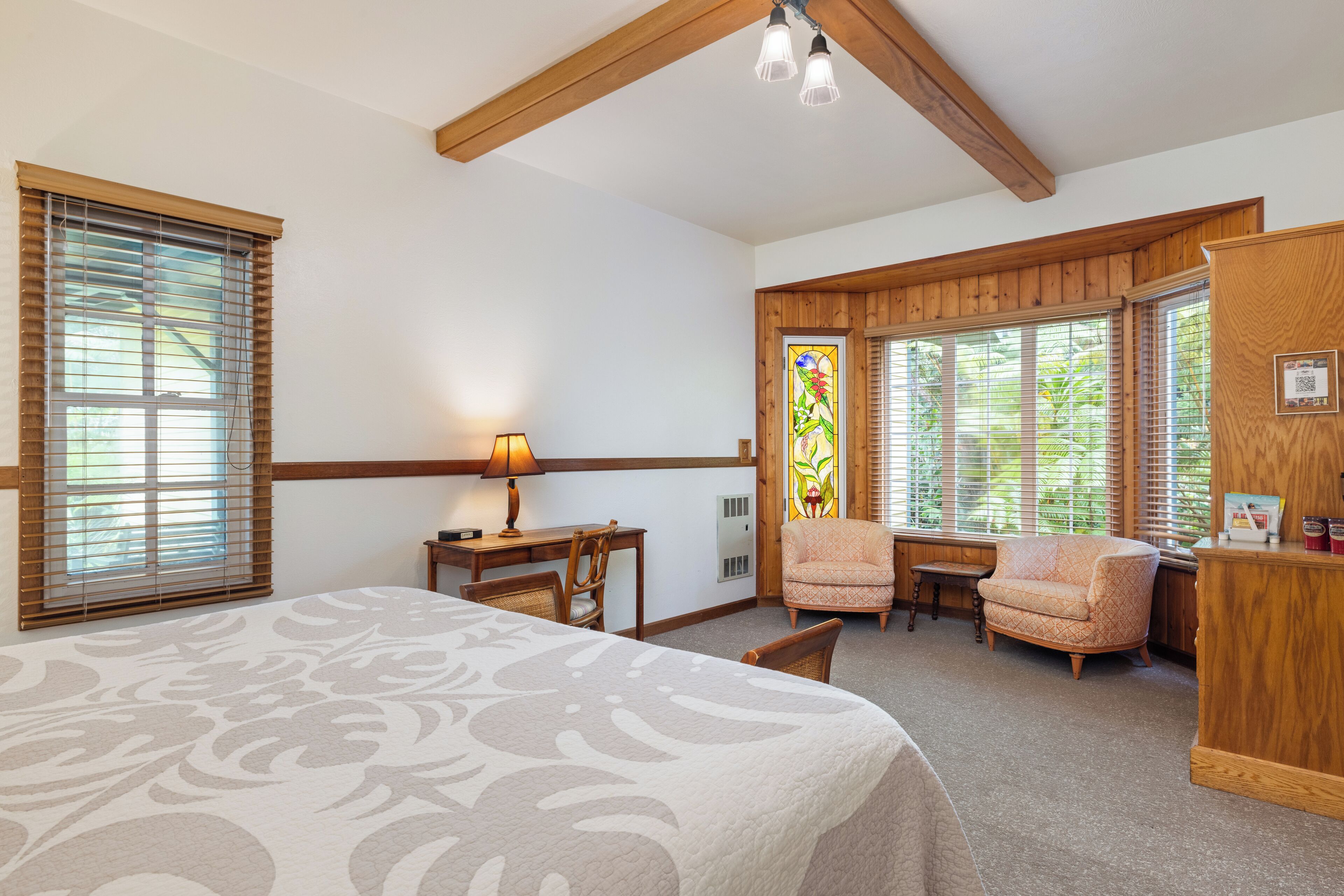 A hotel room with a large bed, a desk, two chairs, a small table, and a wooden cabinet.