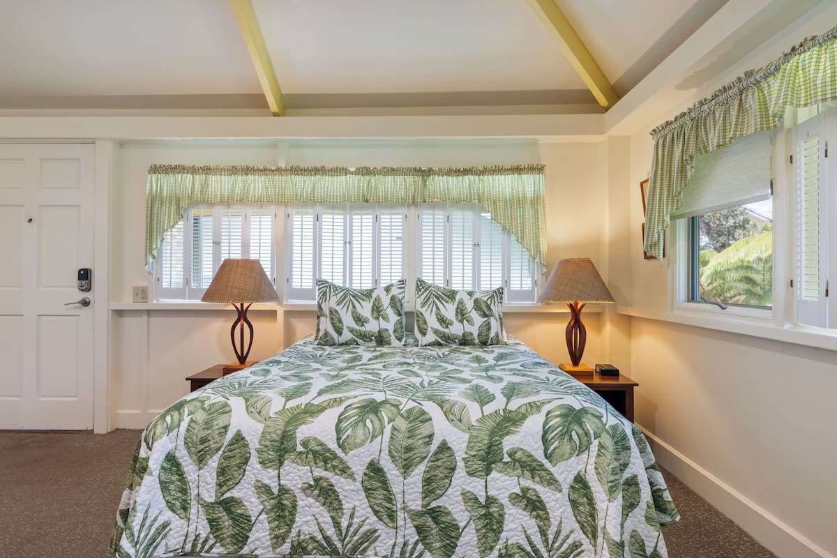 A bedroom with a bed, two bedside lamps, a window with curtains, and a door.